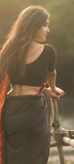 a woman with long hair wearing a black skirt and orange scarf standing on a bridge