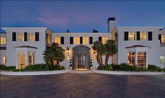 a large white house with palm trees in the front yard at night time and lights on