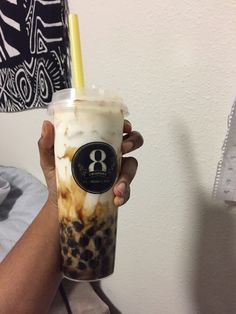 a person holding up a drink in front of a white wall with black and brown designs on it