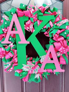 a green and pink wreath with the letter k on it's front door decorated with bows