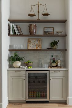 a kitchen with white cabinets and shelves filled with bottles, glasses, fruit and other items