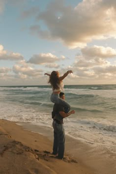 a man carrying a woman on his back at the beach with waves in the background