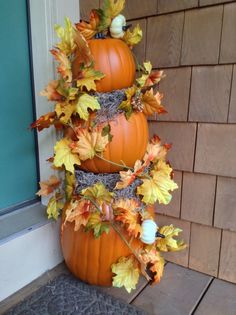 three pumpkins stacked on top of each other in front of a door with leaves around them