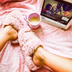 a person laying in bed with their feet on a pink blanket next to a television