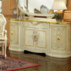 a white and gold dresser with a mirror on it's sideboard next to a chair