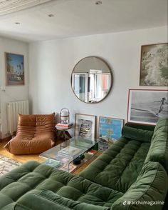 a living room with green couches and pictures on the wall in front of a round mirror