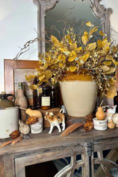 a wooden table topped with a vase filled with yellow flowers and other items next to a mirror