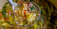 a ladle full of soup with meat and vegetables in it, ready to be eaten