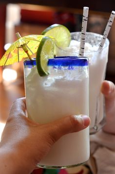 a person holding up a drink with two straws and an umbrella on top of it