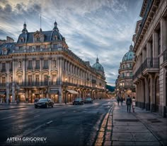 people are walking down the street in front of some old buildings at sunset or dawn