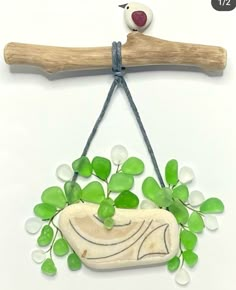 a bird sitting on top of a wooden branch with green leaves and beads hanging from it