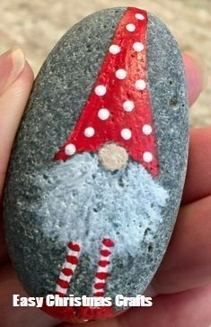 a hand holding a rock with a gnome painted on it's face and wearing a red hat