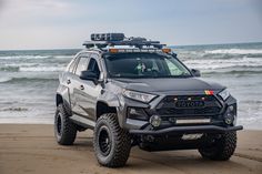 a grey truck parked on top of a sandy beach next to the ocean and waves