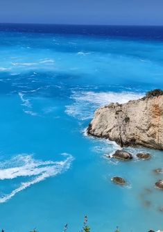 the water is very blue and there are waves coming in from the rocks on the shore