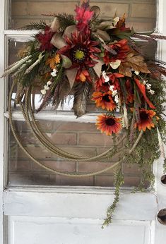 a wreath hanging on the front door of a house decorated with flowers and foliages