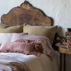 a bed with pillows and blankets on it in front of a wooden headboard,