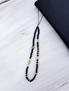 a long black beaded necklace with gold accents on a white surface next to a wallet