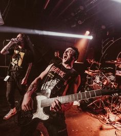 two men on stage with guitars and one is singing into a microphone while the other man plays an electric guitar