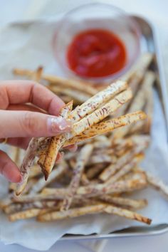 someone is holding up some french fries with ketchup on the side and dipping them in a bowl