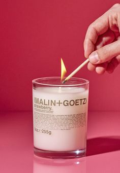 a person lighting a candle with a match stick in front of them on a pink surface