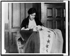 an old black and white photo of a woman sitting at a table with a quilt