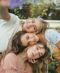 three girls are posing for the camera in front of some plants and trees with their arms around each other