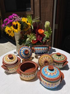 a table topped with lots of colorful pots and vases on top of a white table cloth