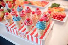 an assortment of ice cream cones with sprinkles and fruit in the background