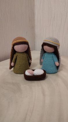 two crocheted dolls sitting next to each other on a white surface with wood planks in the background