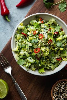 a white bowl filled with green salad next to red chili peppers and lime wedges