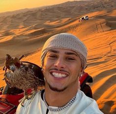 a man in the desert with an eagle on his arm and another vehicle behind him