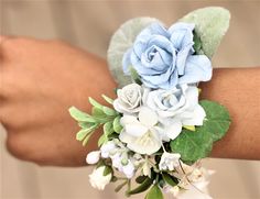 a woman's arm wearing a blue and white wrist corsage with flowers on it