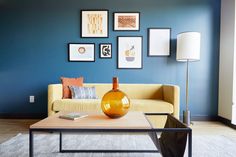 a living room with blue walls and pictures on the wall above the coffee table, along with a yellow couch