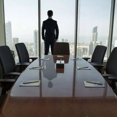 a man standing in front of a conference room table looking out over the cityscape