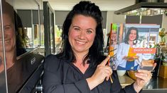 a woman holding up a cookbook in front of her face and smiling at the camera