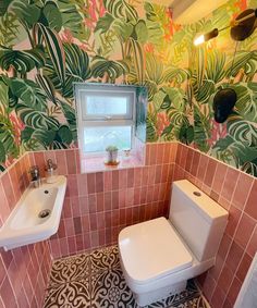 a bathroom with pink and green wallpaper has a toilet, sink, and mirror