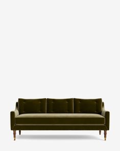 an olive green velvet sofa with wooden legs and arm rests against a white wall, in front of a light grey background