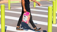 a man walking across a parking lot holding a pink bag