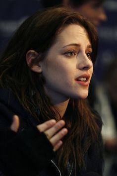 a woman talking into a microphone while wearing a black jacket and holding her hand out