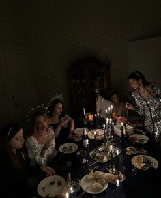 a group of people sitting around a table with food and candles in front of them