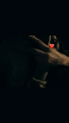 two hands touching each other with a red heart in the middle of their fingers on a black background