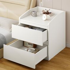 a white night stand with two drawers on top of it and a bed in the background