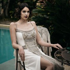 a woman sitting in a chair next to a pool wearing a white dress with sequins on it