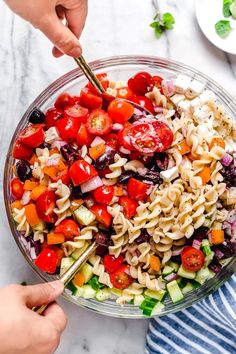 two hands holding a fork over a bowl of pasta salad