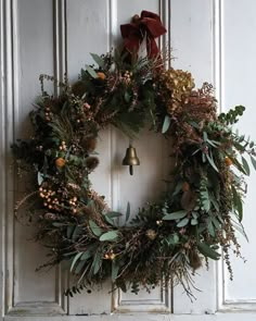 a wreath hanging on the front door of a house with bells and greenery around it