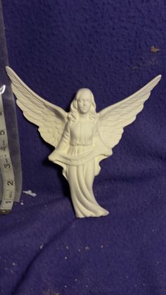 an angel figurine next to a measuring tape on a purple cloth with a ruler in the background