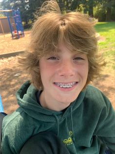 a young boy with blonde hair smiles at the camera while wearing a green hoodie