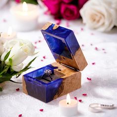 a blue ring box sitting on top of a table next to white flowers and candles