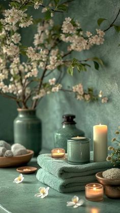 towels, candles and flowers are sitting on a table in front of a green wall