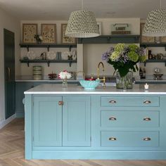 a large kitchen with blue cabinets and white counter tops, two hanging lights above the island